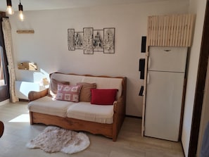 Uma sala de estar aconchegante com um sofá de madeira, uma geladeira branca e uma obra de arte pendurada na parede.