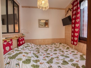 Ein Schlafzimmer mit Bett, Fenster, Spiegel und Fernseher an der Wand.
