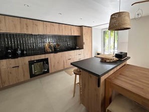 A modern kitchen with a wooden accent wall, a black countertop, and a hanging light fixture. - Spacious apartment - 12 guests (Valloire)