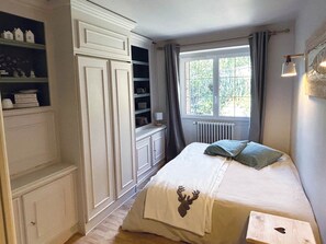 A bedroom with a bed, a window with curtains, built-in shelving, and a radiator. - Spacious apartment - 12 guests (Valloire)