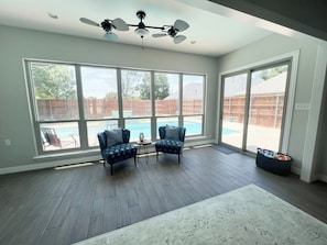 A spacious room with large windows, a ceiling fan, and a view of a backyard with a pool. - Stunning Poolside Retreat w/ Separate Pool House (Irving)