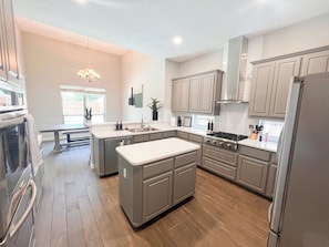 A modern kitchen with a central island, stainless steel appliances, and light wood flooring. - Stunning Poolside Retreat w/ Separate Pool House (Irving)