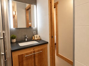 A bathroom with a wooden vanity, a mirror, a sink, and toiletries. - Cozy apartment, mountain view (Méribel)