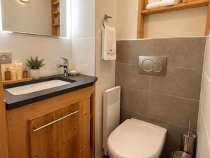 A modern bathroom with a wooden vanity, a white sink, a towel hanging on a rack, and a toilet. - Cozy apartment, mountain view (Méribel)