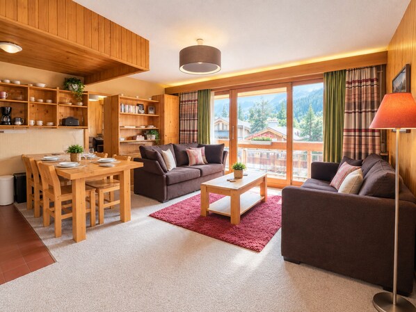A modern living room with a wooden dining area, a sofa set, and a view of the mountains. - Cozy apartment, mountain view (Méribel)