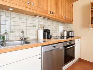 A kitchen with wooden cabinets, a stainless steel dishwasher, an oven, and a tiled backsplash. - Cozy apartment, mountain view (Méribel)