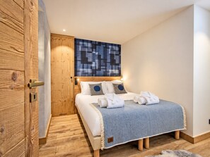 Un dormitorio con un armario de madera, una cama con ropa de cama blanca y detalles azules, y un cuadro abstracto grande sobre la cama.