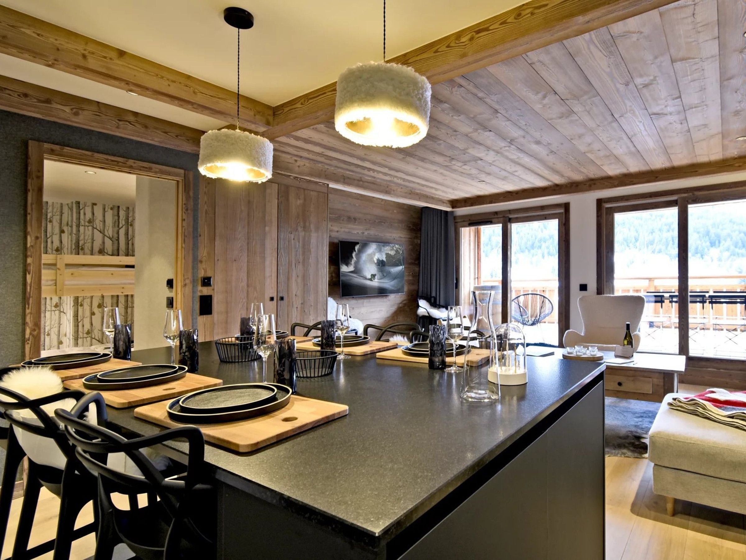 A modern kitchen with a central island, bar stools, and a dining area with a large window.