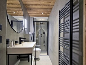 Ein modernes Badezimmer mit Holzboden, einer Duschkabine aus Glas, einem weißen Waschbecken und einer Toilette.