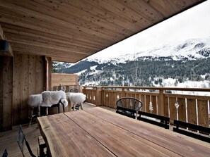 Eine Holzterrasse mit Tisch und Stühlen mit Blick auf eine verschneite Berglandschaft.