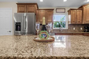 A kitchen with granite countertops, stainless steel appliances, wooden cabinets, and a view of greenery outside. - La Tortuga! Gulf Access Pool, Spa, Dock & Tiki hut on canal. Close to beaches (Cape Coral)