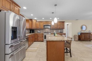 A modern kitchen with stainless steel appliances, wooden cabinets, and a central island. - La Tortuga! Gulf Access Pool, Spa, Dock & Tiki hut on canal. Close to beaches (Cape Coral)
