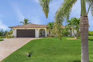A residential property with a garage, a well-maintained lawn, and palm trees. - La Tortuga! Gulf Access Pool, Spa, Dock & Tiki hut on canal. Close to beaches (Cape Coral)