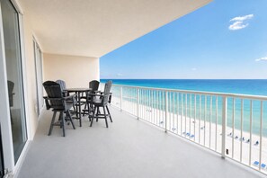 A balcony with a table and chairs, overlooking a beach with a white railing. - Refined Gulf Front Family Retreat with Pool, Stunning Balcony Views, & Bunk Nook (Panama City Beach)