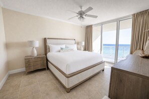 A hotel room with a large bed, two bedside tables, a ceiling fan, and a view of the ocean. - Refined Gulf Front Family Retreat with Pool, Stunning Balcony Views, & Bunk Nook (Panama City Beach)