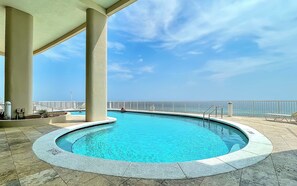 A swimming pool with a view of the ocean, surrounded by a covered area with columns and a tiled floor. - Refined Gulf Front Family Retreat with Pool, Stunning Balcony Views, & Bunk Nook (Panama City Beach)