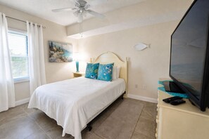 Ein Schlafzimmer mit einem Bett, einem Deckenventilator, einem Gemälde, einer Lampe und einem Fernseher.