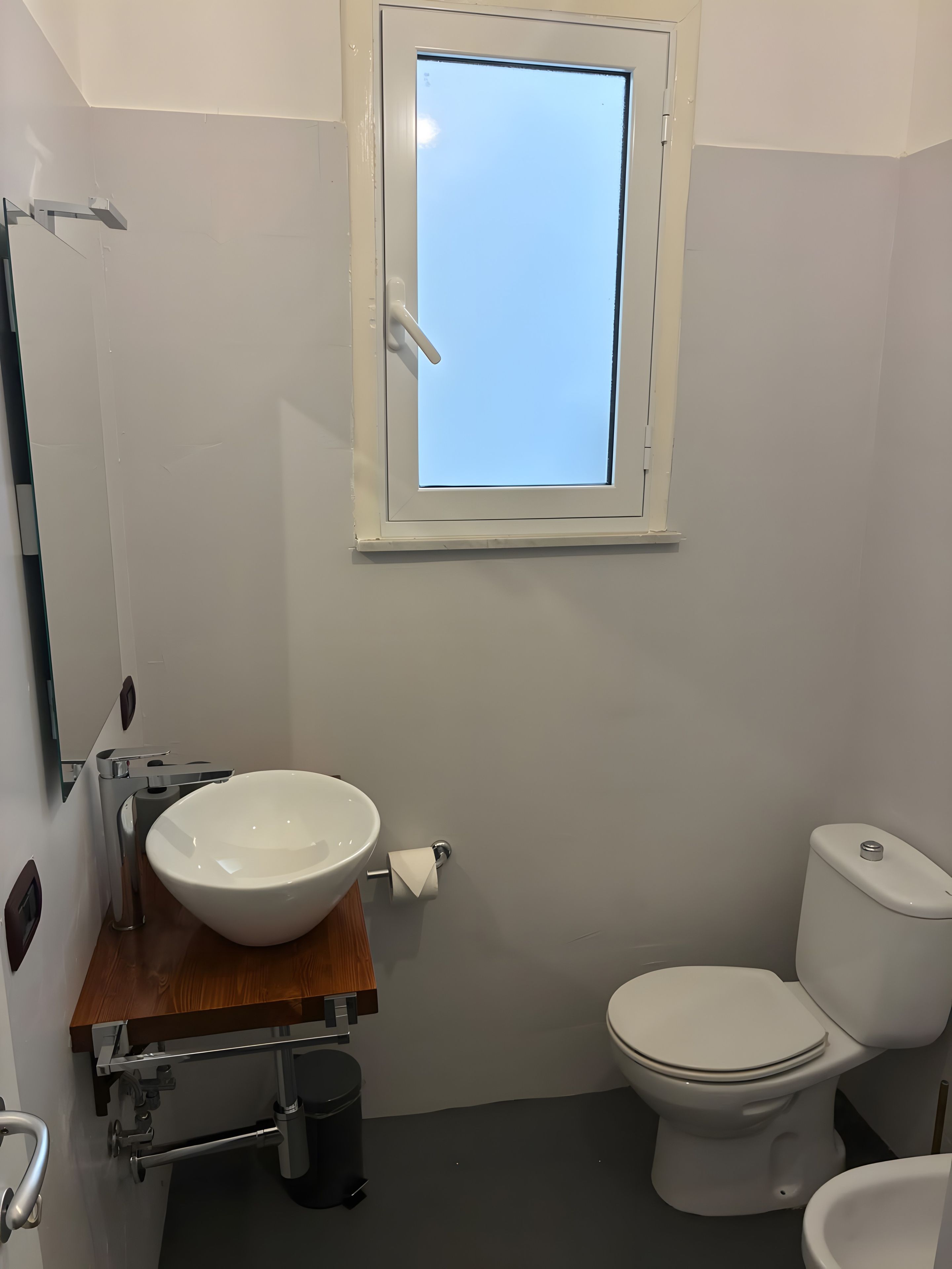 A bathroom with a white sink, toilet, and a window above the sink.
