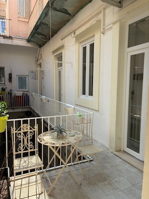 Un balcon avec une chaise et une table en métal, un pot de fleurs et une fenêtre donnant sur un immeuble.