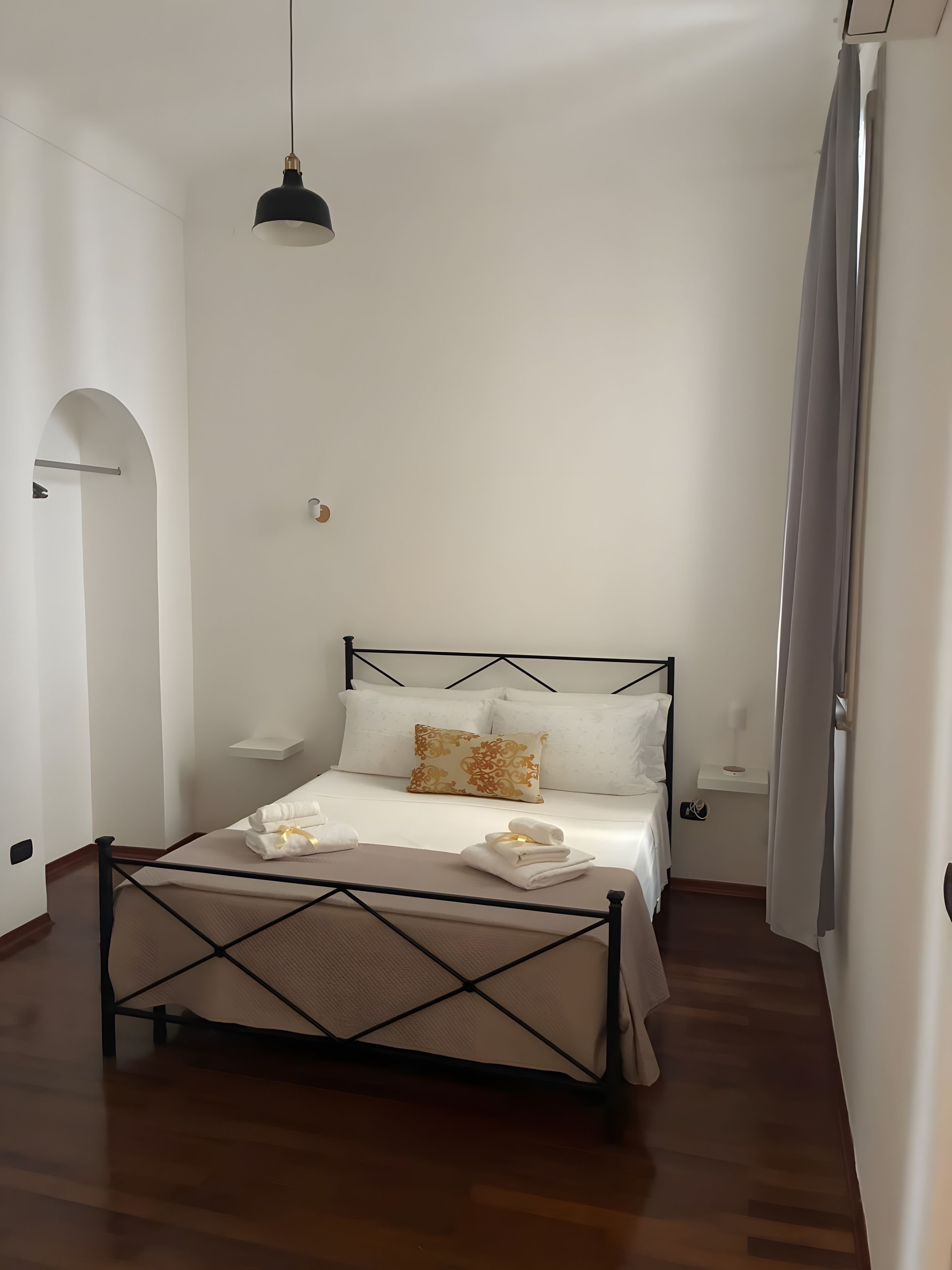 A bedroom with a bed, a hanging light fixture, and a wooden floor.