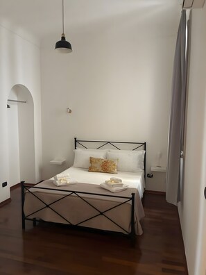 A bedroom with a bed, a hanging light fixture, and a wooden floor. - Room 'Camera Nix' with Wi-Fi and Air Conditioning (Siracusa)