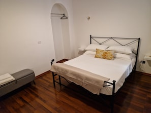 Une chambre à coucher avec un lit, un banc et une étagère fixée au mur.