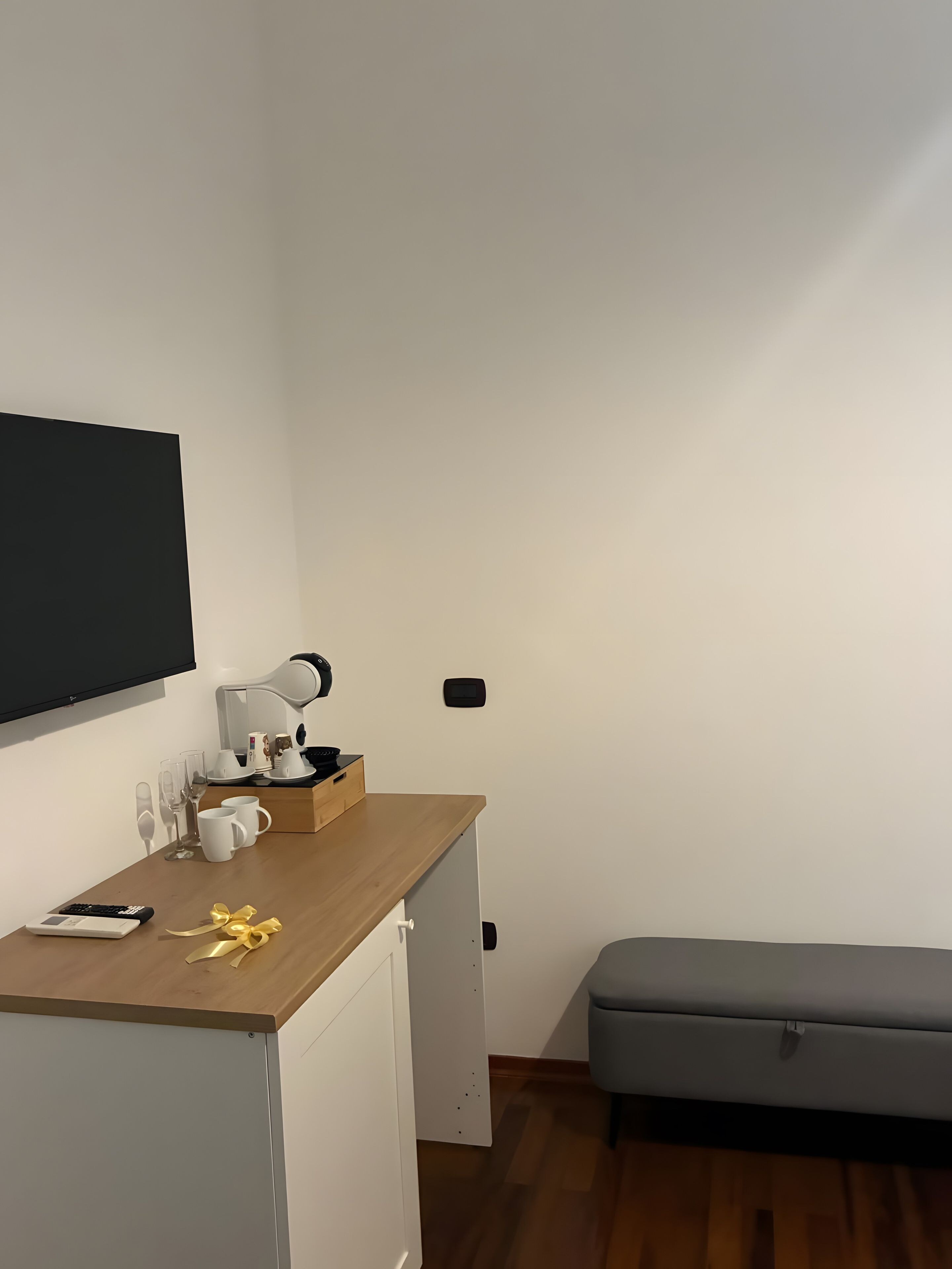 A small room with a wooden desk, a television mounted on the wall, a bench, and a door with a handle.