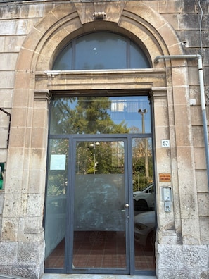 A building entrance with a large arched doorway, a glass door, and a metal number plate. - Room 'Camera Nix' with Wi-Fi and Air Conditioning (Siracusa)