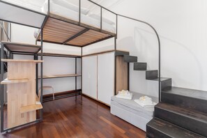 A modern interior with a loft bed, open shelving, a small seating area, and a staircase. - Apartment 'Iris' with balcony, Wi-Fi and air conditioning (Siracusa)