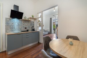 A modern kitchen with grey cabinets, a wooden countertop, and a built-in stove. There is a dining area with a round wooden table and grey upholstered chairs. - Apartment 'Iris' with balcony, Wi-Fi and air conditioning (Siracusa)