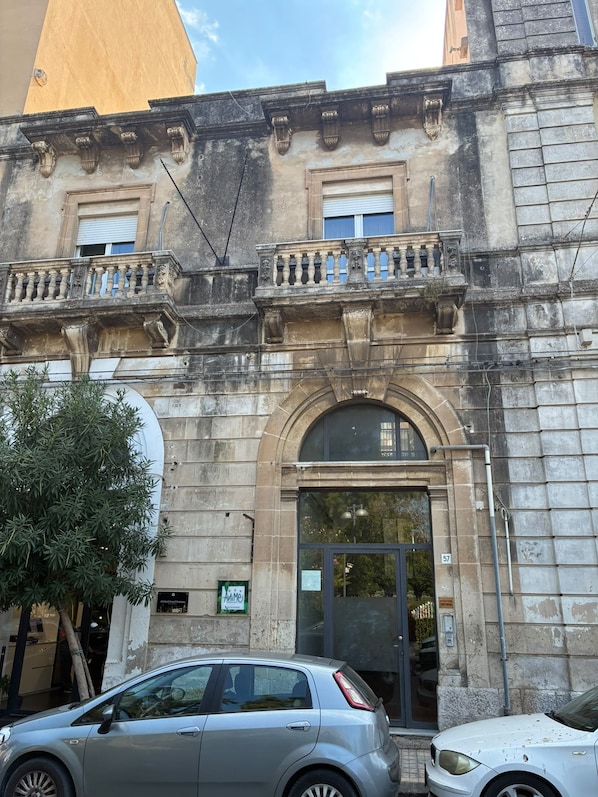 Ein historisches Gebäude mit einer Stein-Fassade, einem Balkon mit Brüstung und einem großen Rundbogen-Eingang.