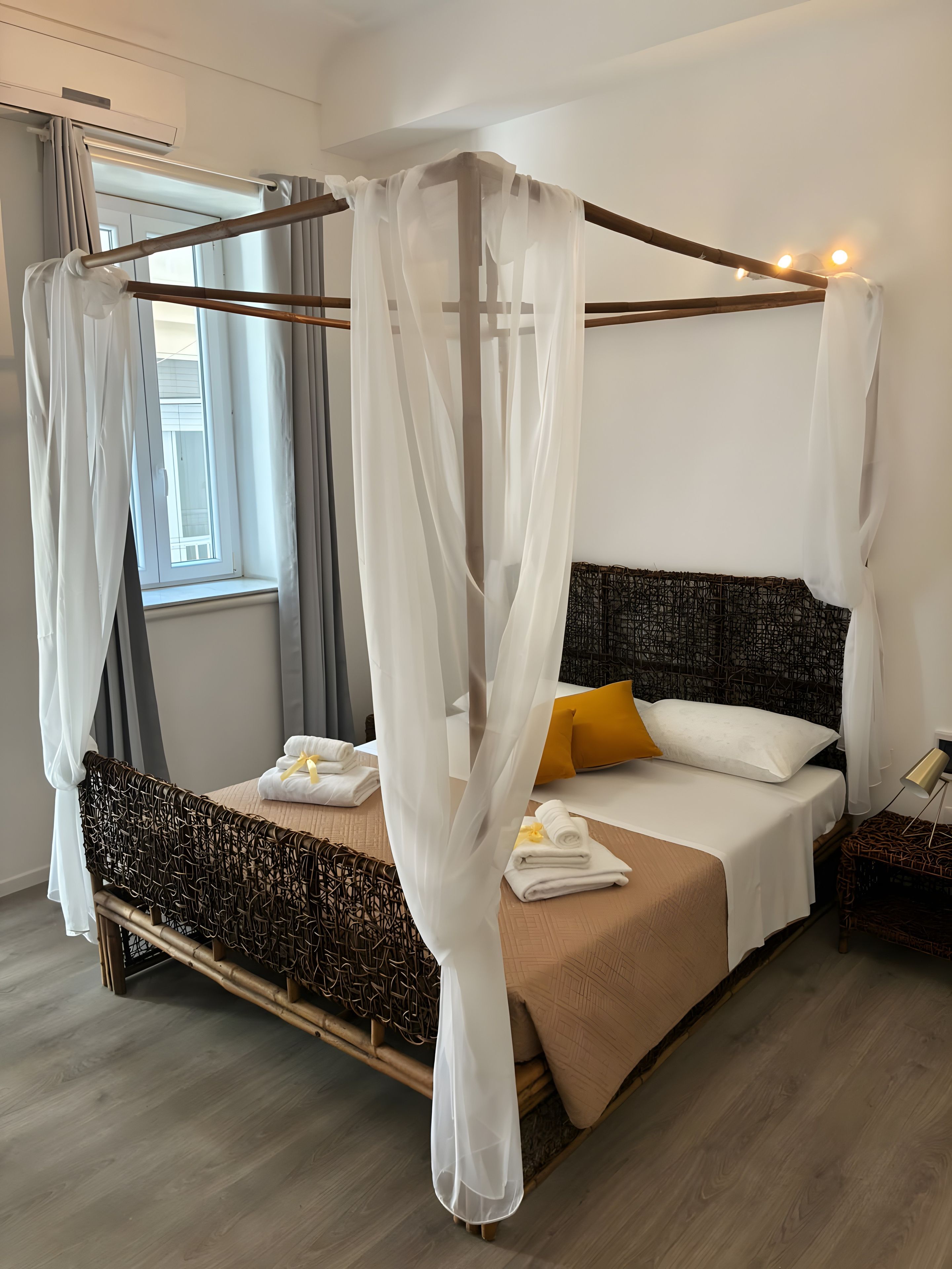 A four-poster bed with white drapes, a patterned headboard, and a bedside table with a lamp.