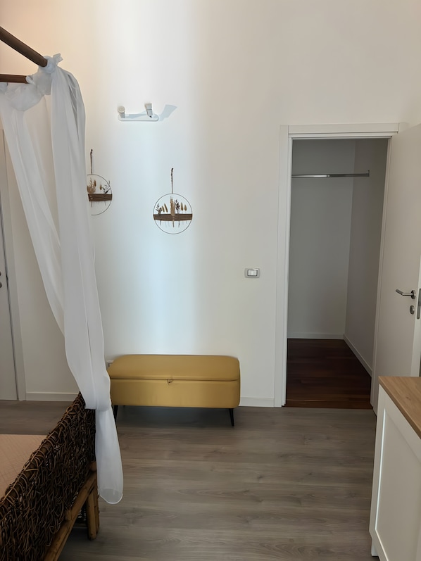 A bedroom with a canopy bed, a bench, a wall-mounted shelf, and a door leading to another room. - Room 'Camera Clio' with Balcony, Wi-Fi and Air Conditioning (Siracusa)