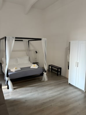 A bedroom with a four-poster bed, a bedside table, a bench, and a wardrobe. - Room 'Camera Dea' with Balcony, Wi-Fi and Air Conditioning (Siracusa)