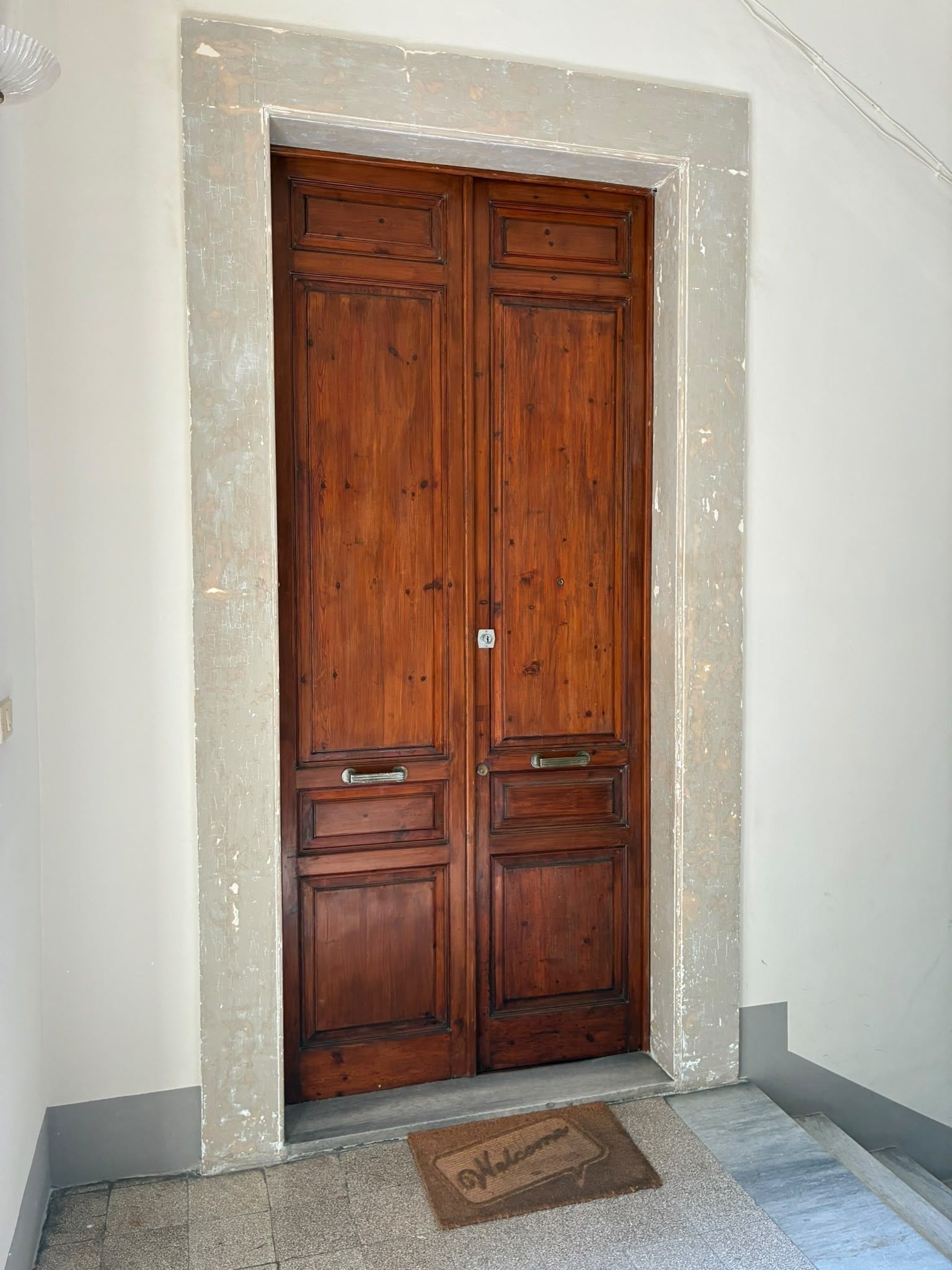 A wooden double door with a doormat in front.