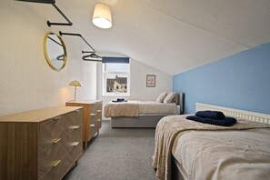 Ein Schlafzimmer mit Bett, Kommode, Spiegel, Fenster und einer Wandlampe.