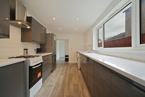 A modern kitchen with a stove, oven, microwave, and a window overlooking a residential area. - Cleethorpes 3-Bed House | Garden | Sleeps 6 (Cleethorpes)