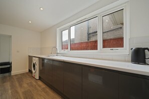 Eine moderne Küche mit integriertem Waschmaschine, einem großen Fenster und einem Wasserkocher auf der Arbeitsfläche.