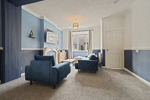 A room with a fireplace, two sofas, a television, and a door leading to another room. - Cleethorpes 3-Bed House | Garden | Sleeps 6 (Cleethorpes)