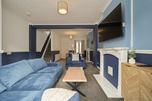 A living room with a blue sofa set, a wooden coffee table, a TV mounted on the wall, and a fireplace. - Cleethorpes 3-Bed House | Garden | Sleeps 6 (Cleethorpes)
