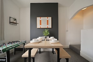 A dining area with a table set for four, a foosball table, and a framed abstract painting on the wall. - Grimsby 3-Bed House | Free Parking | Foosball (Grimsby)