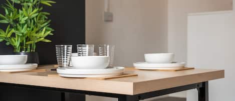 Una mesa de comedor con platos y tazones blancos, vasos y una planta en maceta.