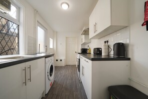 A modern kitchen with a built-in washer, a coffee machine, and a kettle on the countertop. - Grimsby 3-Bed House | Free Parking | Foosball (Grimsby)