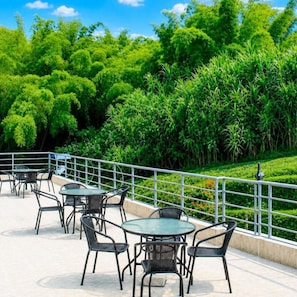 An outdoor patio area with tables and chairs, surrounded by lush greenery and a metal railing.