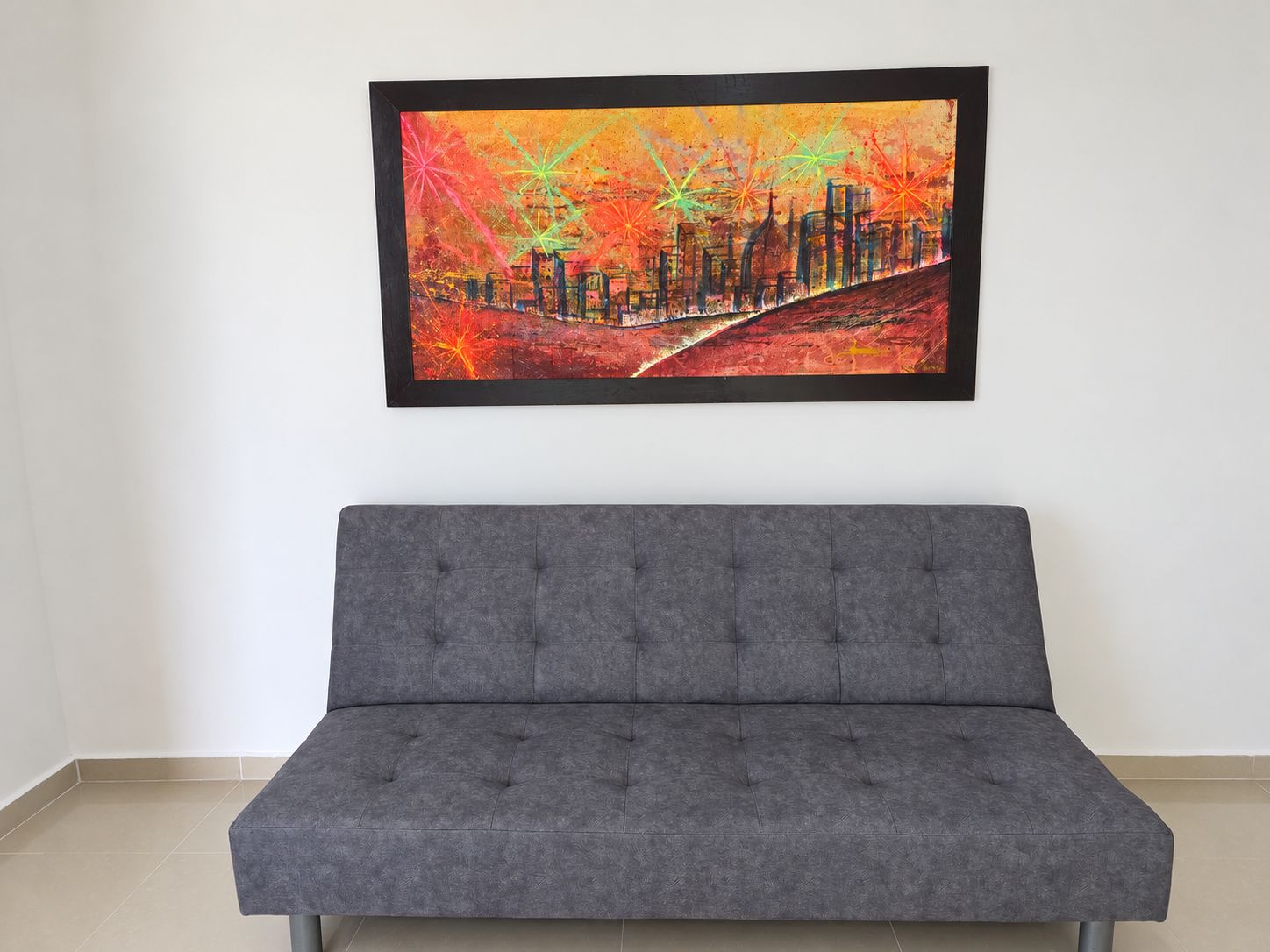 Un sofá gris en una habitación con un cuadro abstracto y colorido en la pared.