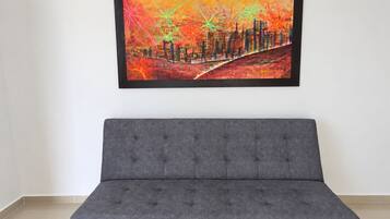Un sofá gris en una habitación con un cuadro abstracto y colorido en la pared.