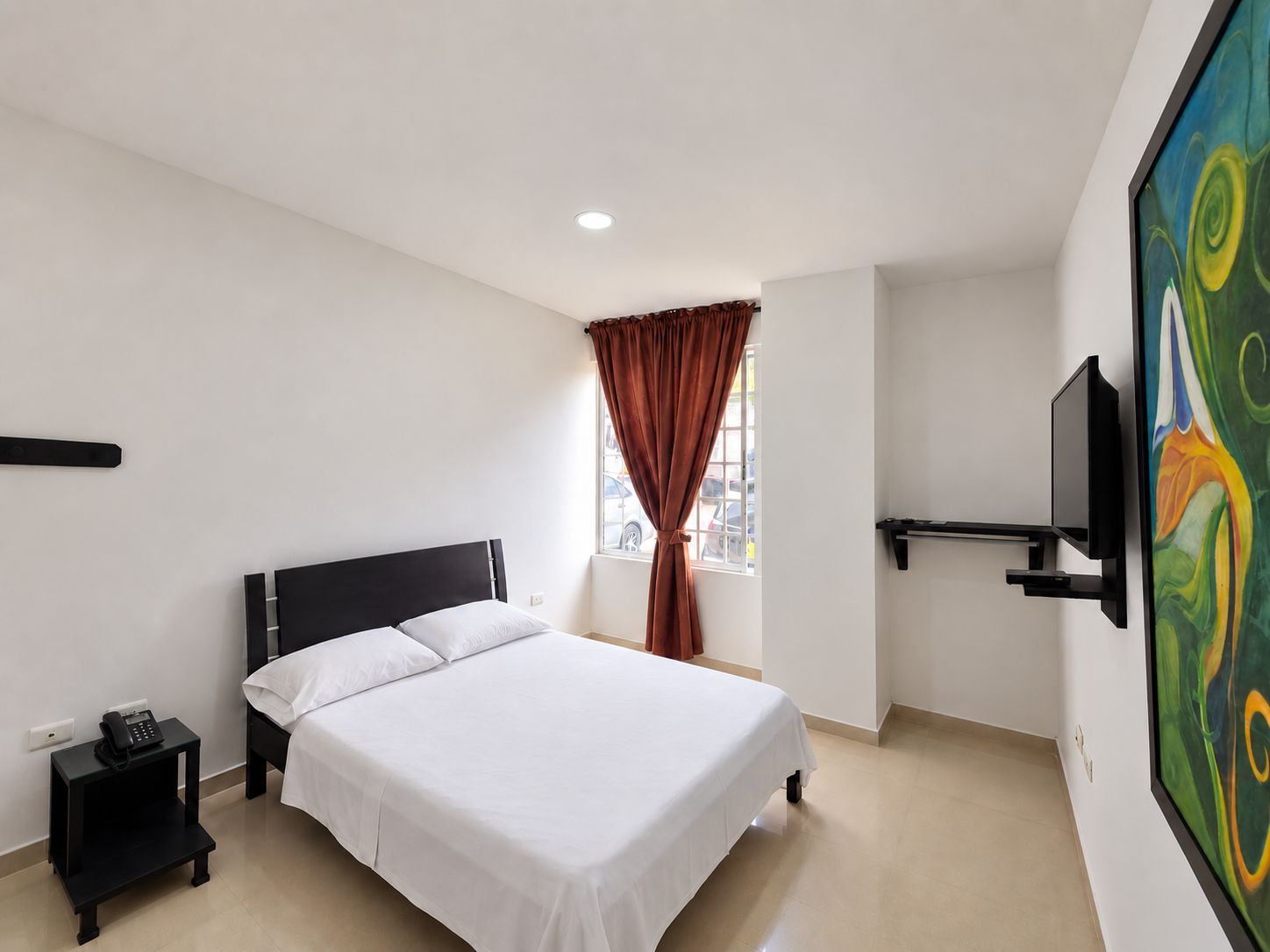 A hotel room with a bed, a nightstand, a telephone, a window with curtains, and a painting on the wall.