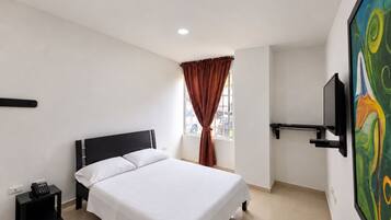 A hotel room with a bed, a nightstand, a telephone, a window with curtains, and a painting on the wall.