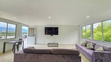 Una sala de estar amplia con un televisor de pantalla plana grande montado en la pared, un sofá y un comedor con sillas.