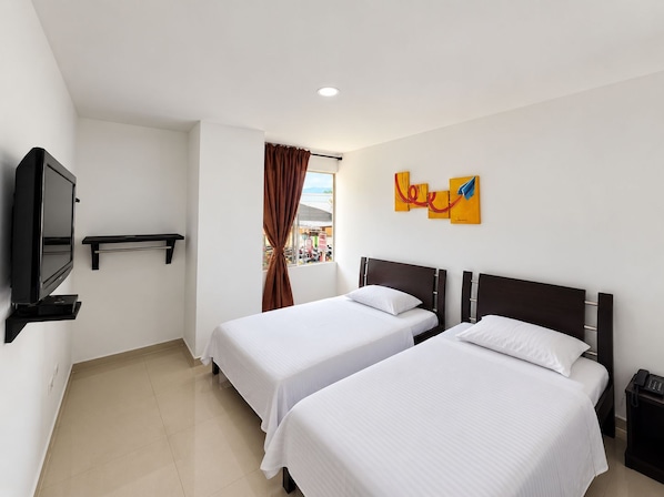 A hotel room with two beds, a TV, a window with curtains, and artwork on the wall.
